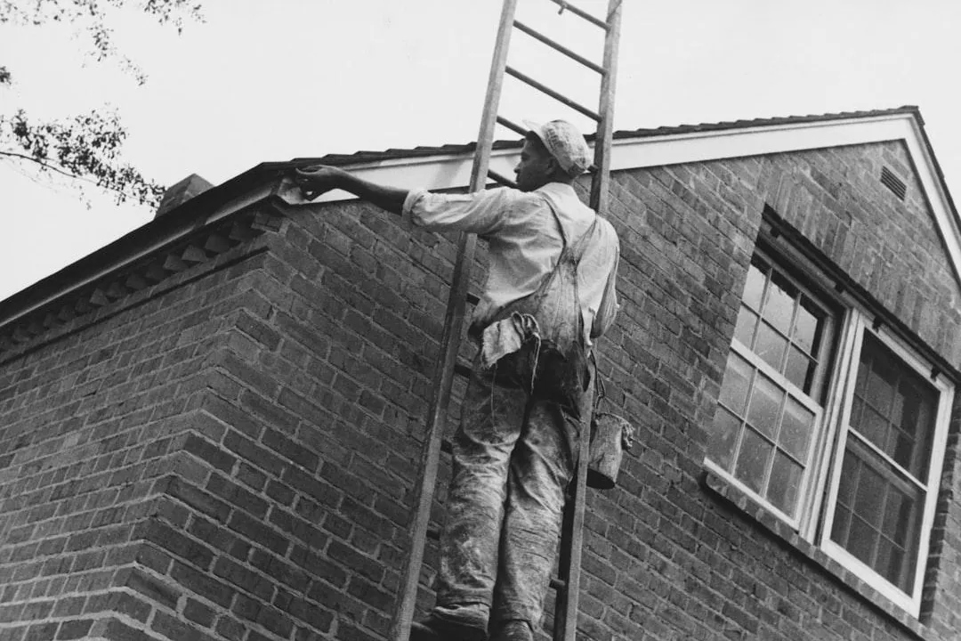 Painter on a ladder painting the trim of a brick house