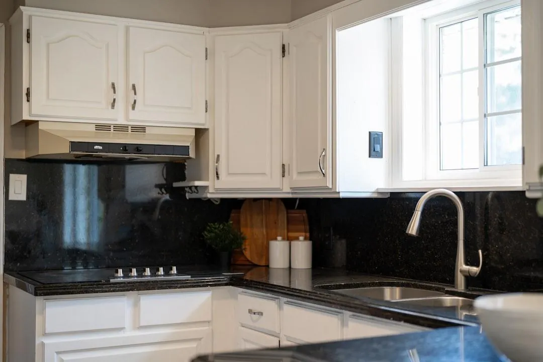 Kitchen with freshly painted white cabinets and a dark granite backsplash
